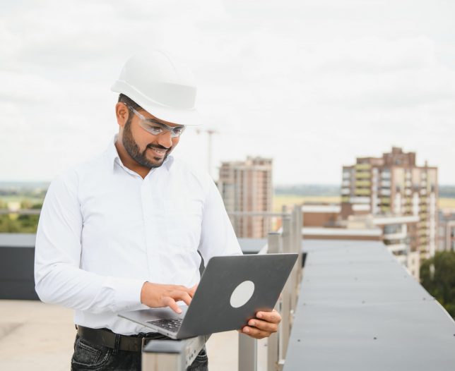 Indian male engineer wearing helmet at construction site. Copy space. Real estate.