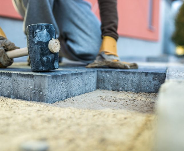 Workman tamping down a new paving brick with a mallet.